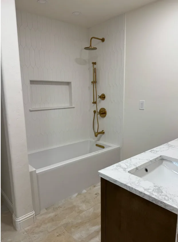 Bathroom remodel with a white picket tile tub surround, brushed gold shower fixtures, recessed niche and marble-top vanity.