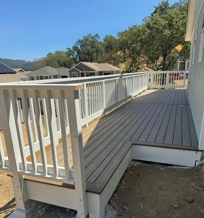 Gray composite deck with a white railing and built-in bench, looking out over oak-covered foothills, built by Sequoia Builders & Remodel.