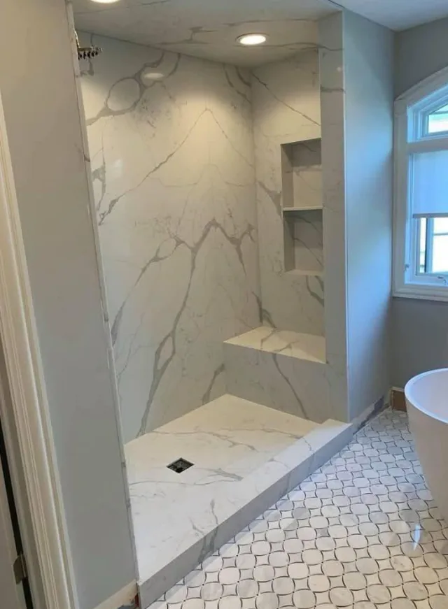 Walk-in marble slab shower with a built-in bench and recessed niche shelving, from a bathroom remodel by Sequoia Builders & Remodel.