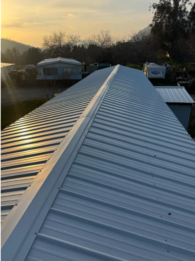 Ribbed metal roof panels running to the ridge on a completed re-roof, photographed at sunset below the Sierra foothills.