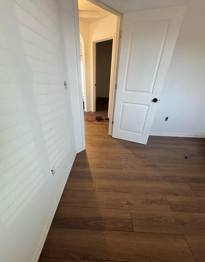 Interior of a home mid-remodel with new wide-plank flooring, freshly painted walls and a new two-panel interior door.