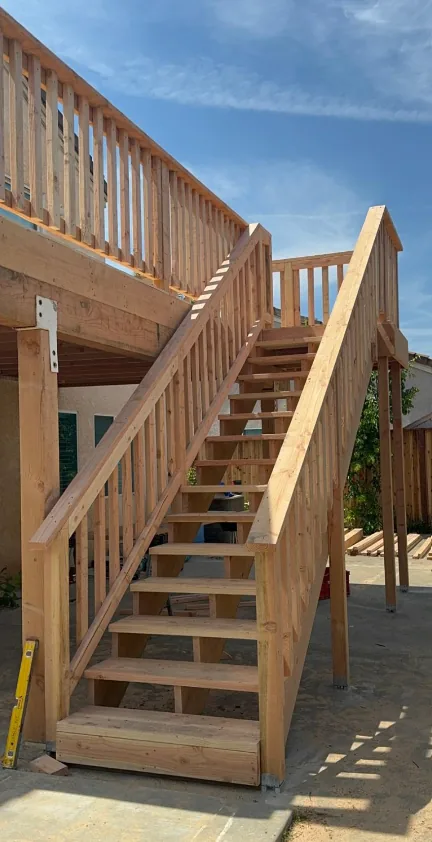 Newly framed exterior wood staircase with cut stringers and matching balusters rising to a raised deck.